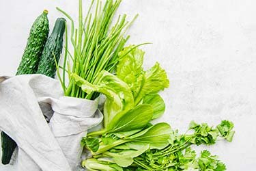 green vegetables in a white cotton shopping bag laying on a grey marble background