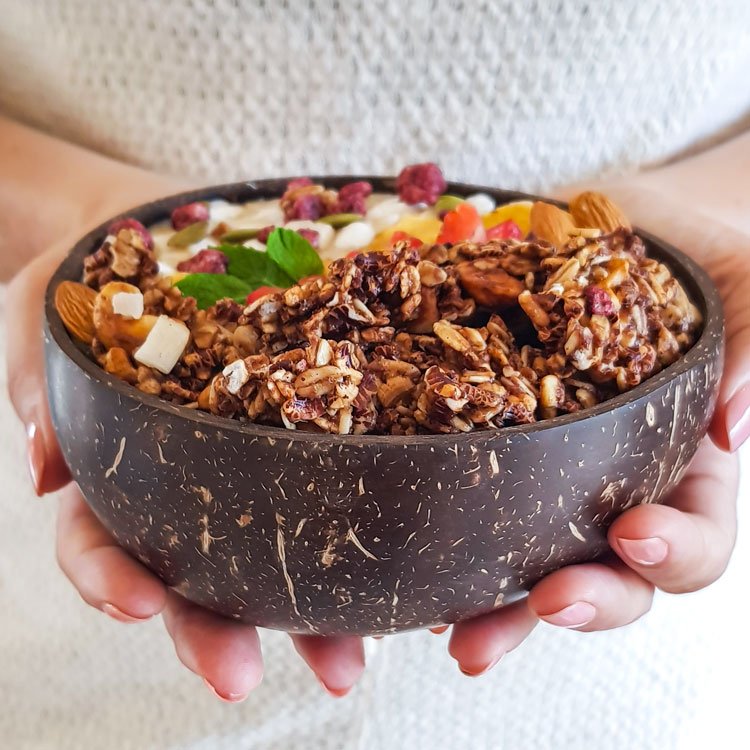 hands holding a granola filled coconut bowl