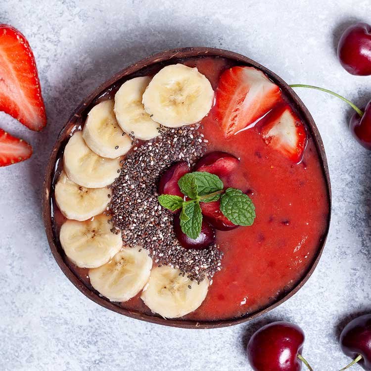 red smoothie topped with chia seeds, banana and cherries. Served in a coconut bowl.
