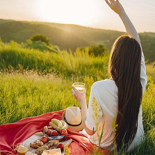 A brunette woman sits having a picnic in a field.