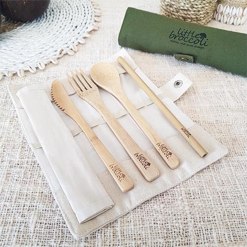A natural colour bamboo cutlery pouch is open on the table and the cutlery set lays on top. There is a green pouch in the background.